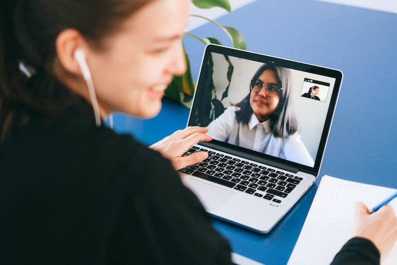 A woman taking notes while video chatting to another woman.