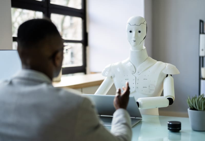 A robot taking notes on a laptop while a person talks to it.