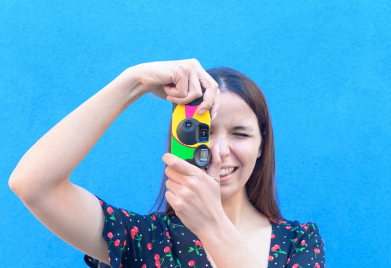 A woman in a casual outfit taking pictures with a disposable camera.
